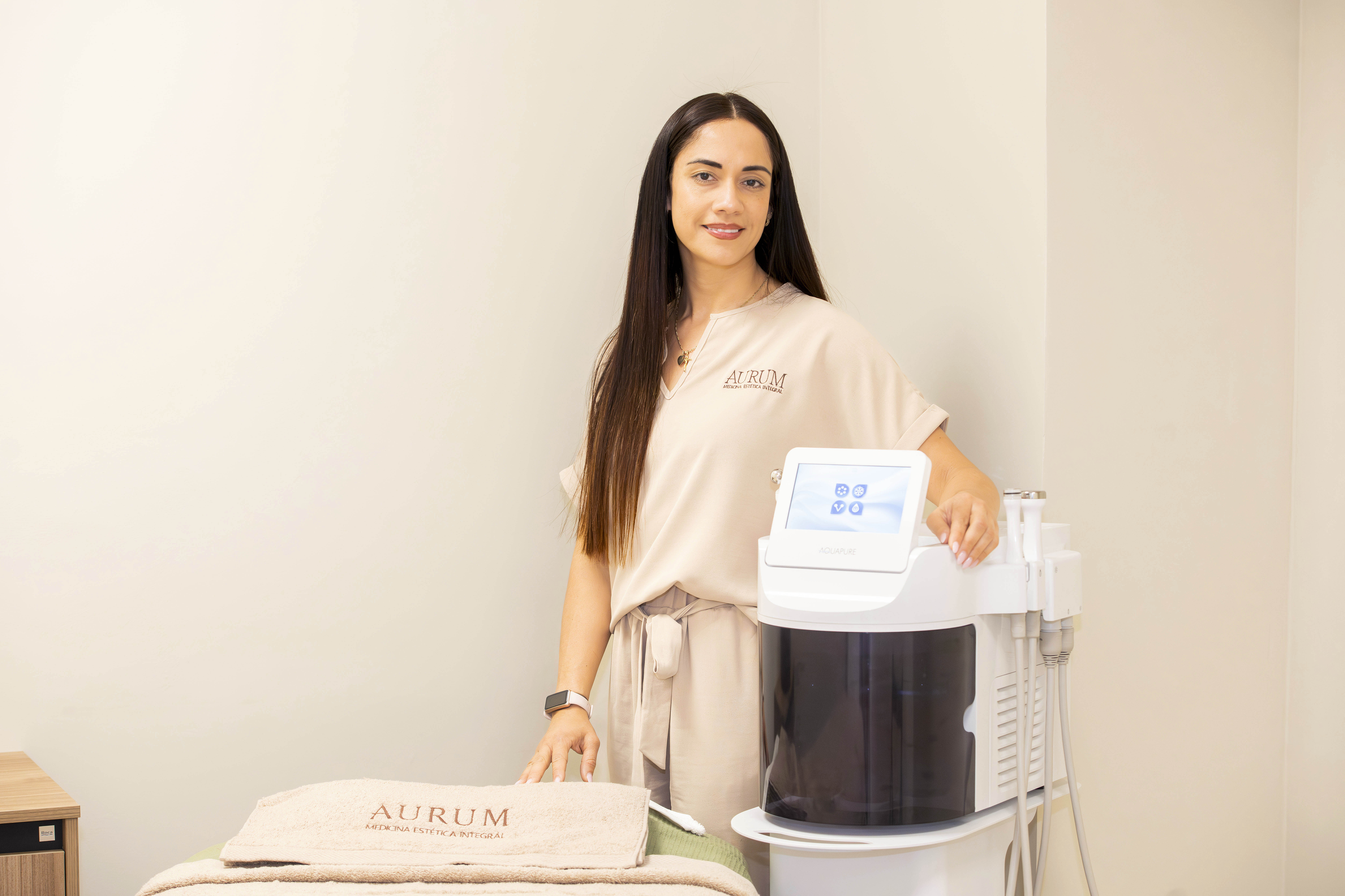 Una profesional de la estética sonríe junto a un equipo de tratamiento AquaPure en un ambiente de clínica moderna.